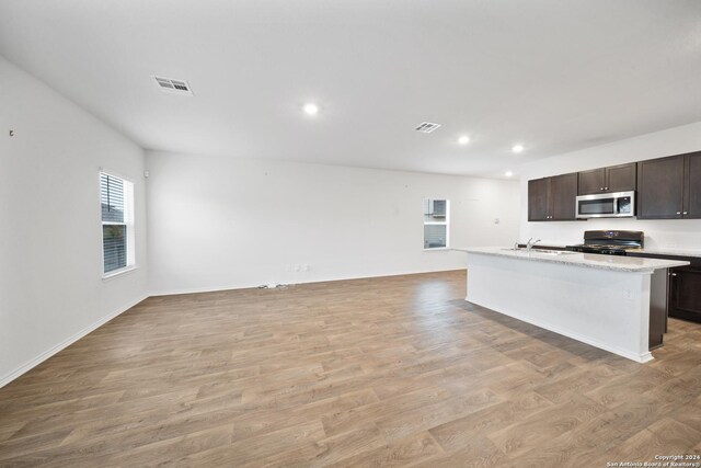 kitchen with black stove, dark brown cabinets, a kitchen island with sink, sink, and light hardwood / wood-style floors