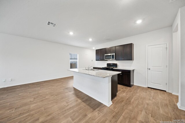 kitchen featuring light hardwood / wood-style flooring, an island with sink, gas stove, light stone counters, and dark brown cabinetry