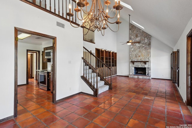 interior space with a fireplace, dark tile patterned flooring, ceiling fan with notable chandelier, and high vaulted ceiling