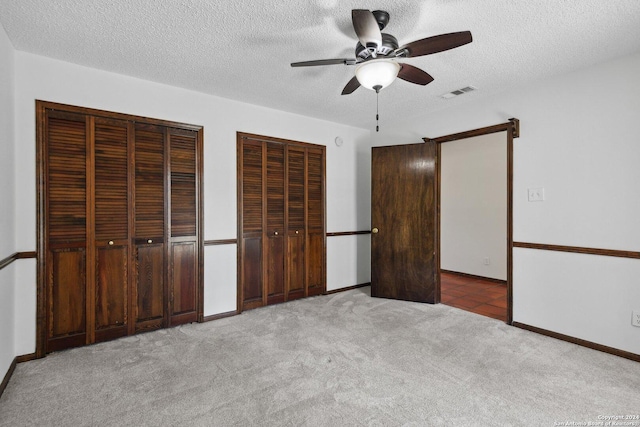 unfurnished bedroom with ceiling fan, a textured ceiling, light carpet, and two closets