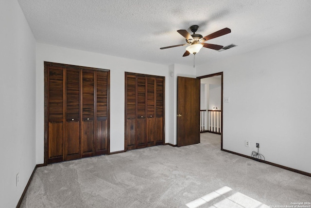 unfurnished bedroom featuring a textured ceiling, light colored carpet, ceiling fan, and multiple closets