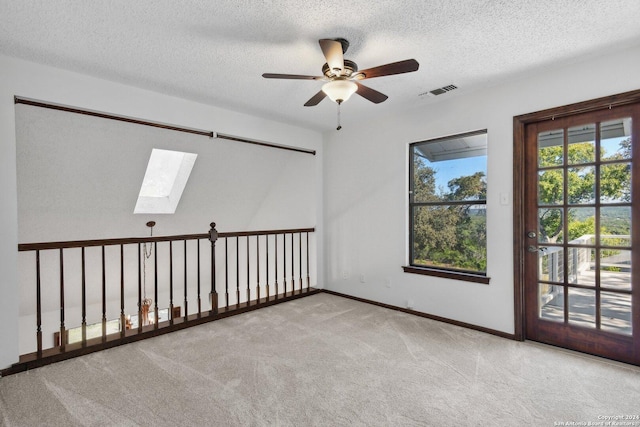 carpeted empty room featuring a textured ceiling, a skylight, and ceiling fan