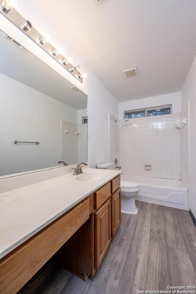 full bathroom with hardwood / wood-style floors, tiled shower / bath combo, toilet, and vanity