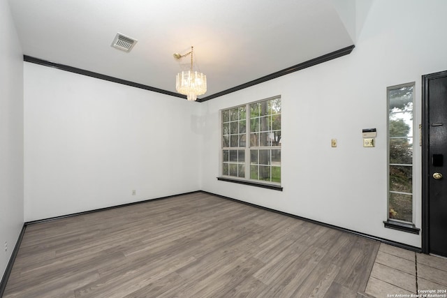 empty room with wood-type flooring, crown molding, and a chandelier