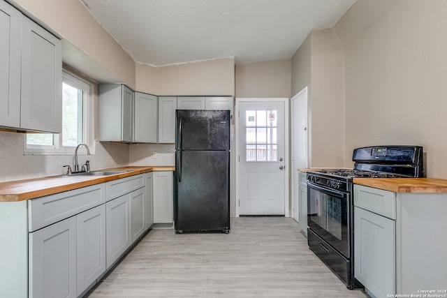 kitchen with butcher block counters, sink, light hardwood / wood-style flooring, lofted ceiling, and black appliances