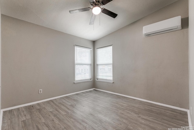 unfurnished room featuring a wall mounted air conditioner, hardwood / wood-style flooring, vaulted ceiling, and ceiling fan