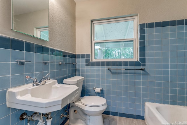 bathroom featuring a bath, wood-type flooring, toilet, and tile walls