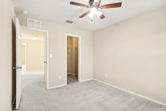 unfurnished bedroom with a walk in closet, a closet, ceiling fan, and light colored carpet