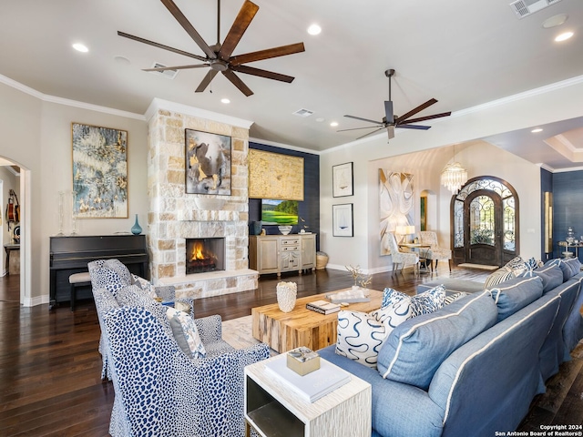 living room with crown molding, a stone fireplace, dark wood-type flooring, and ceiling fan with notable chandelier