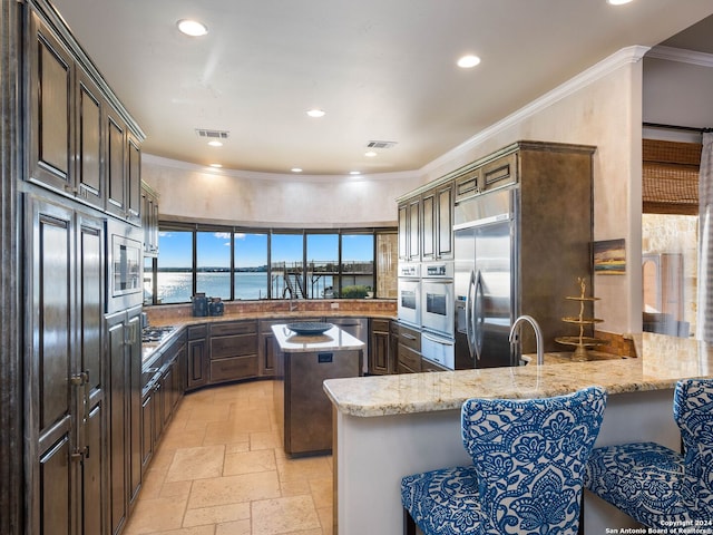 kitchen featuring a center island, light stone counters, built in appliances, kitchen peninsula, and a water view