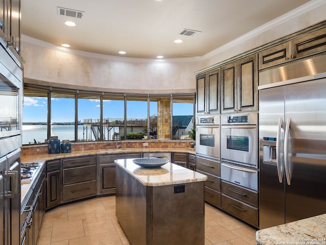 kitchen with light stone countertops, dark brown cabinetry, stainless steel appliances, a water view, and a kitchen island