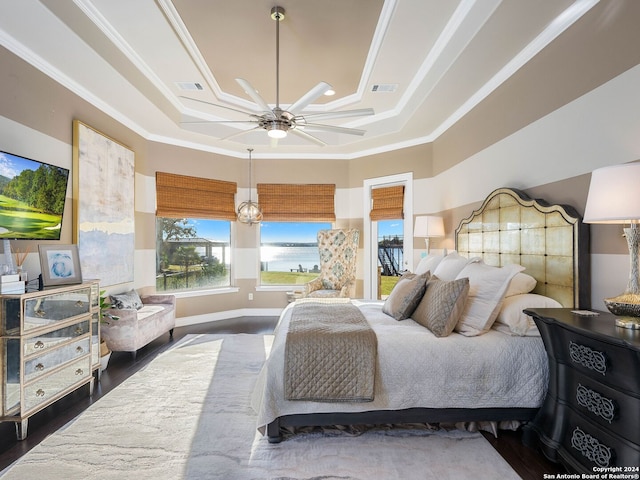 bedroom featuring dark wood-type flooring, a raised ceiling, a water view, crown molding, and ceiling fan