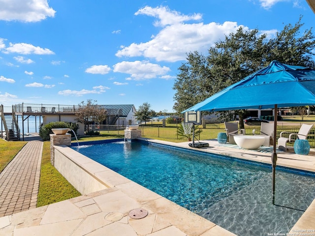 view of pool with pool water feature, a water view, a patio area, and a lawn