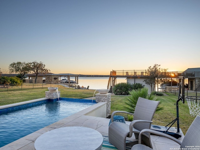 pool at dusk with a yard, pool water feature, and a water view