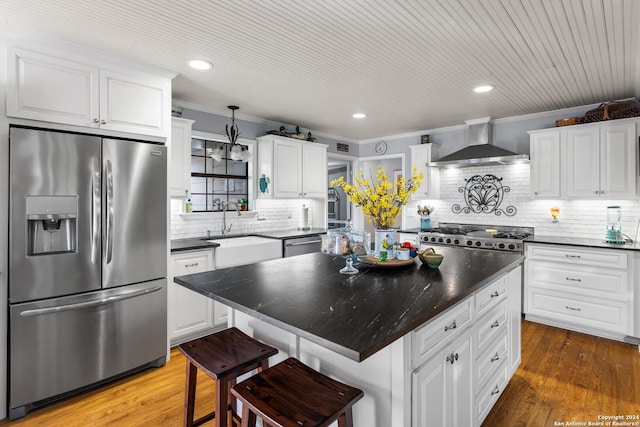 kitchen with appliances with stainless steel finishes, dark hardwood / wood-style flooring, sink, wall chimney range hood, and a kitchen island