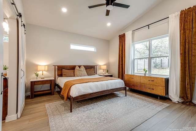 bedroom with ceiling fan, radiator heating unit, a barn door, light hardwood / wood-style floors, and vaulted ceiling