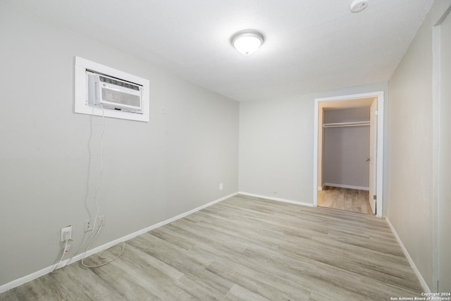 unfurnished bedroom with an AC wall unit, a walk in closet, a closet, and light hardwood / wood-style flooring