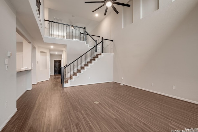 unfurnished living room with ceiling fan, dark wood-type flooring, and a high ceiling