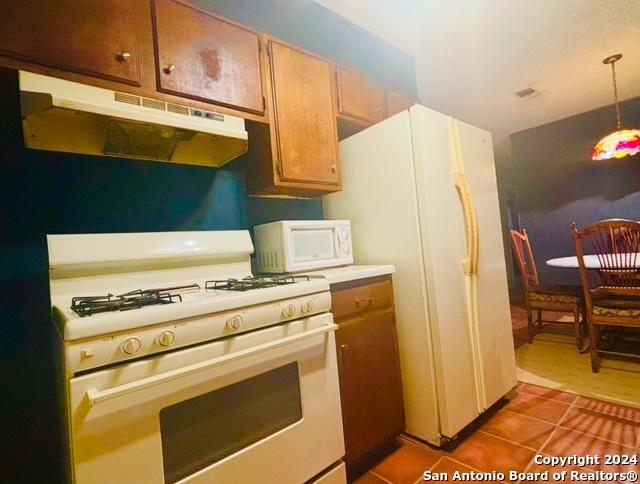 kitchen featuring white appliances, decorative light fixtures, and dark tile patterned flooring