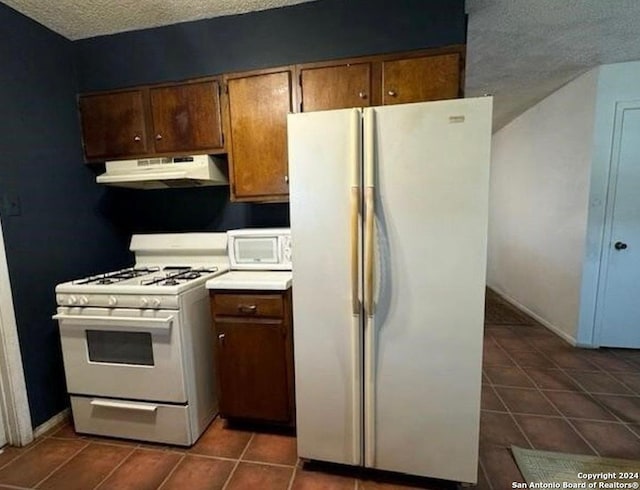 kitchen with a textured ceiling, white appliances, and dark tile patterned floors