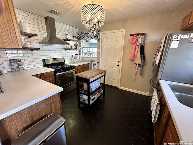 kitchen with decorative backsplash, wall chimney exhaust hood, stainless steel appliances, pendant lighting, and a notable chandelier