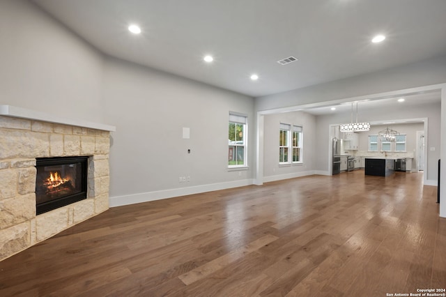 unfurnished living room with a stone fireplace, dark hardwood / wood-style flooring, and sink