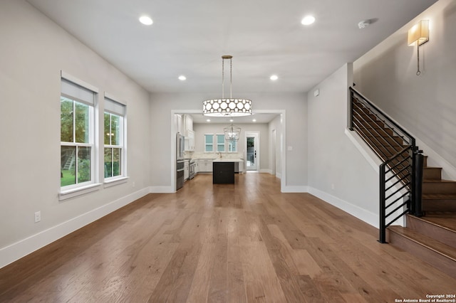 unfurnished living room with light wood-type flooring, an inviting chandelier, and sink