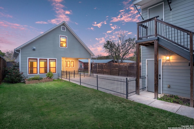 back house at dusk featuring a lawn