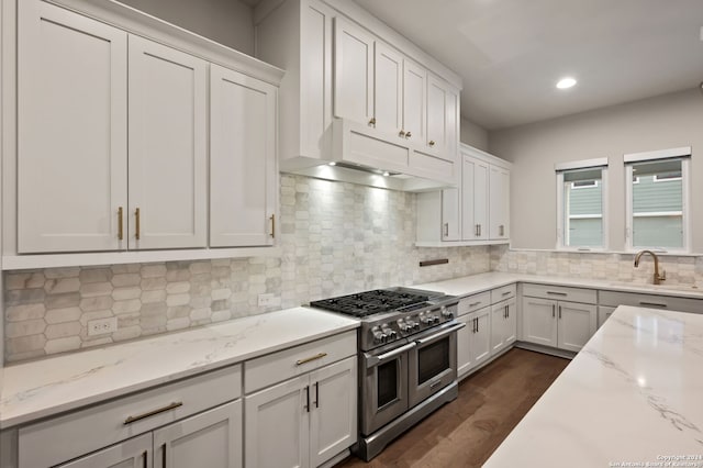 kitchen with light stone countertops, dark hardwood / wood-style flooring, white cabinetry, and double oven range