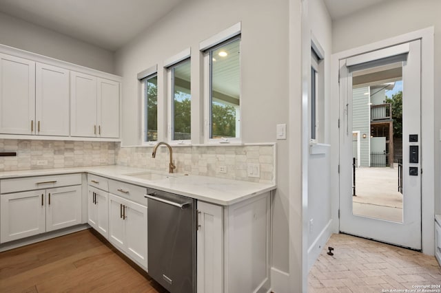 kitchen featuring tasteful backsplash, white cabinetry, stainless steel dishwasher, and sink