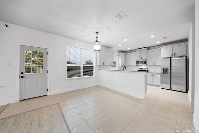 kitchen featuring light stone counters, kitchen peninsula, decorative light fixtures, light tile patterned floors, and appliances with stainless steel finishes