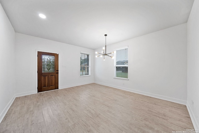 spare room with a wealth of natural light, a notable chandelier, and light wood-type flooring