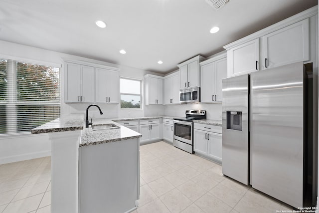 kitchen featuring kitchen peninsula, light stone counters, stainless steel appliances, sink, and white cabinetry