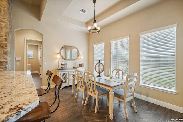 dining space with a notable chandelier, a raised ceiling, and dark parquet floors