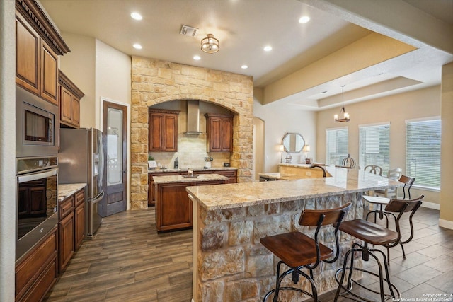 kitchen with tasteful backsplash, wall chimney exhaust hood, stainless steel appliances, dark wood-type flooring, and a large island with sink