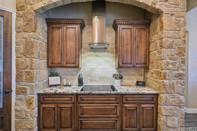 kitchen with black electric stovetop, wall chimney exhaust hood, light stone counters, and tasteful backsplash