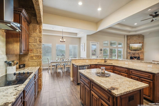 kitchen featuring pendant lighting, dark wood-type flooring, ceiling fan with notable chandelier, wall chimney range hood, and a large island