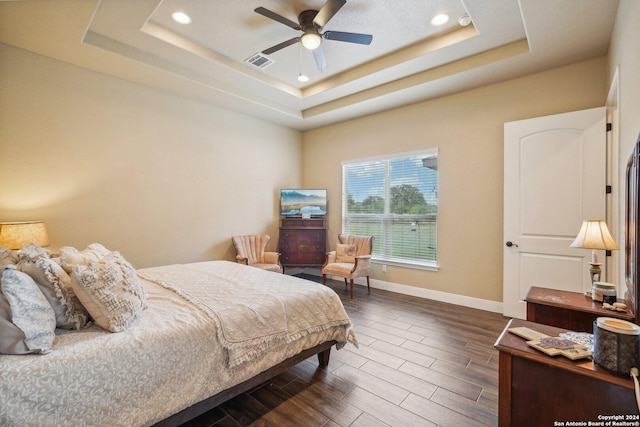 bedroom with a raised ceiling, ceiling fan, and dark hardwood / wood-style flooring