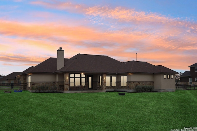 back house at dusk featuring a lawn