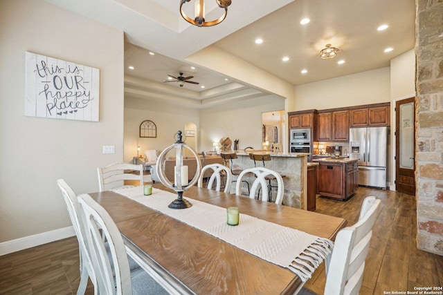 dining area featuring ceiling fan with notable chandelier, a tray ceiling, and dark wood-type flooring