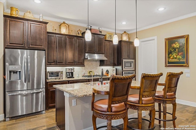 kitchen with dark brown cabinetry, stainless steel appliances, a kitchen island with sink, decorative light fixtures, and a breakfast bar area