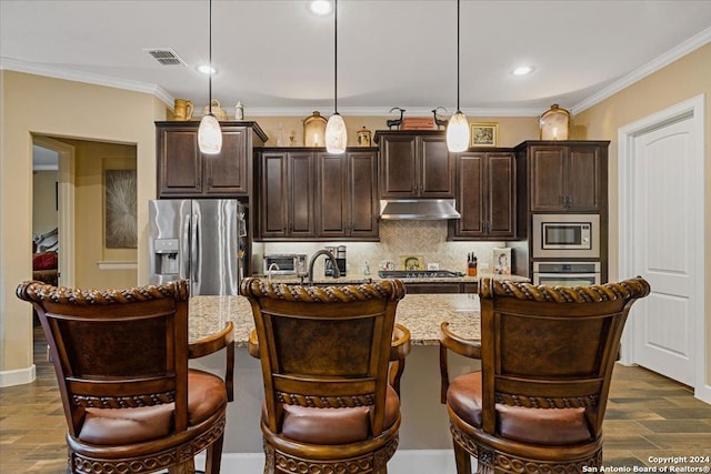 kitchen with a kitchen bar, appliances with stainless steel finishes, dark brown cabinets, pendant lighting, and a center island with sink