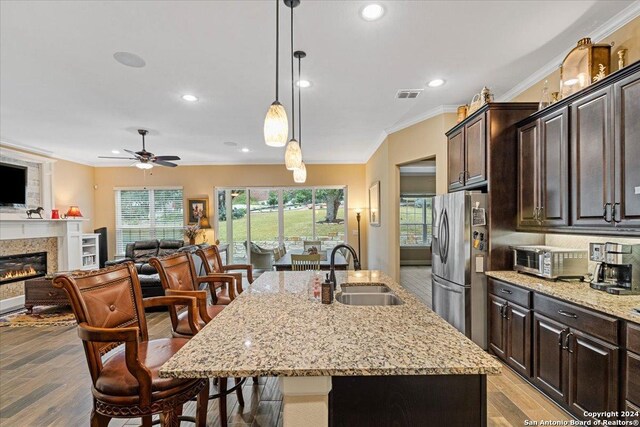 kitchen with dark brown cabinetry, sink, light hardwood / wood-style flooring, stainless steel refrigerator with ice dispenser, and a center island with sink