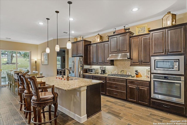 kitchen with dark brown cabinetry, stainless steel appliances, a kitchen breakfast bar, an island with sink, and decorative light fixtures