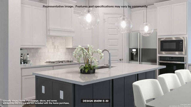 kitchen with sink, a kitchen island with sink, stainless steel appliances, decorative backsplash, and white cabinets