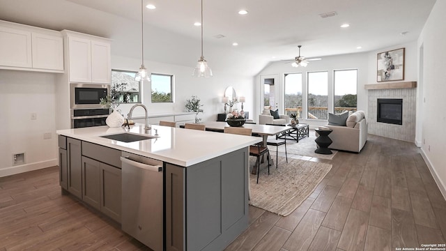 kitchen featuring wood finished floors, a kitchen island with sink, stainless steel appliances, a fireplace, and a sink