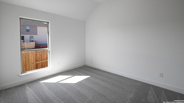 carpeted empty room featuring vaulted ceiling and baseboards