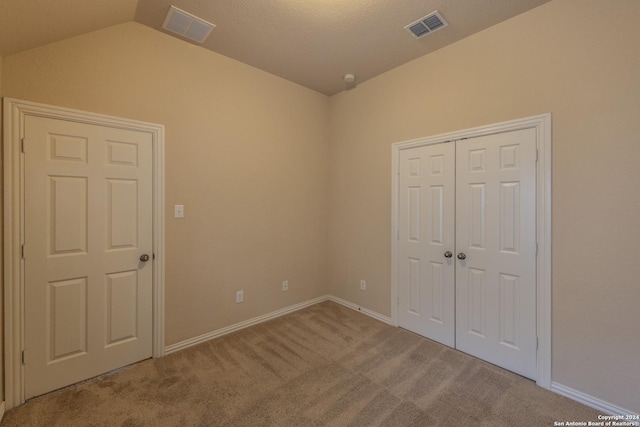 unfurnished bedroom featuring light carpet, a closet, and lofted ceiling