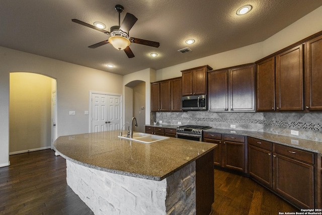 kitchen featuring appliances with stainless steel finishes, sink, dark stone countertops, dark hardwood / wood-style floors, and an island with sink