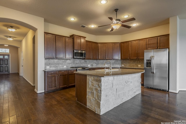 kitchen with sink, dark hardwood / wood-style flooring, backsplash, an island with sink, and appliances with stainless steel finishes